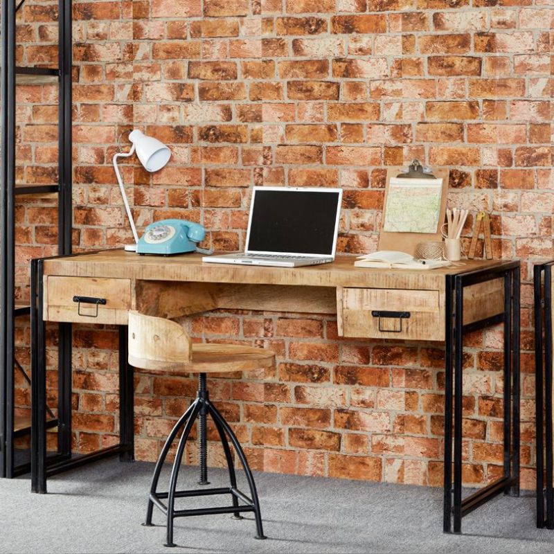 A modern workspace with a laptop, desk, and chair against a brick wall.