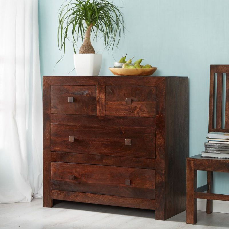 A wooden chest of drawers in a room with a vase and a lamp.