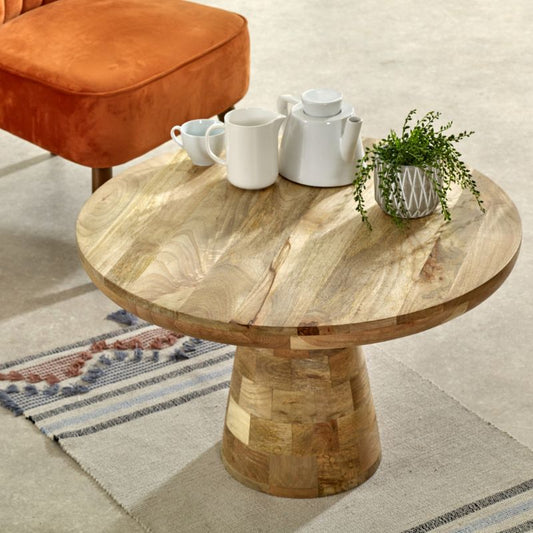 A round wooden table with a coffee cup and a chair.