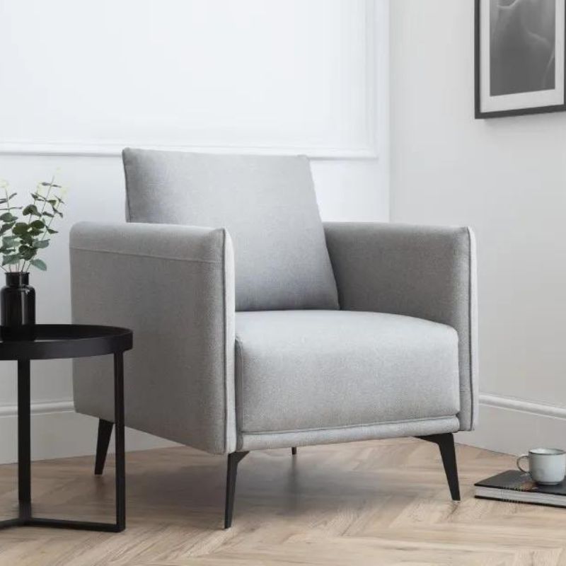 A grey chair positioned in a room featuring a clean, white wall as the backdrop, creating a minimalist aesthetic.