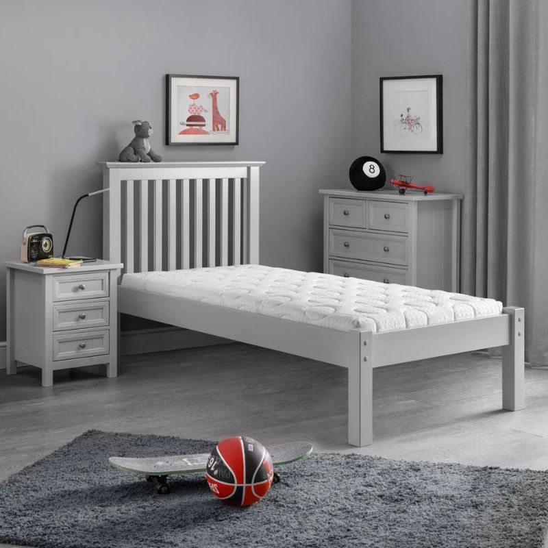 A grey bedroom featuring a bed, a nightstand, and a skateboard leaning against the wall.