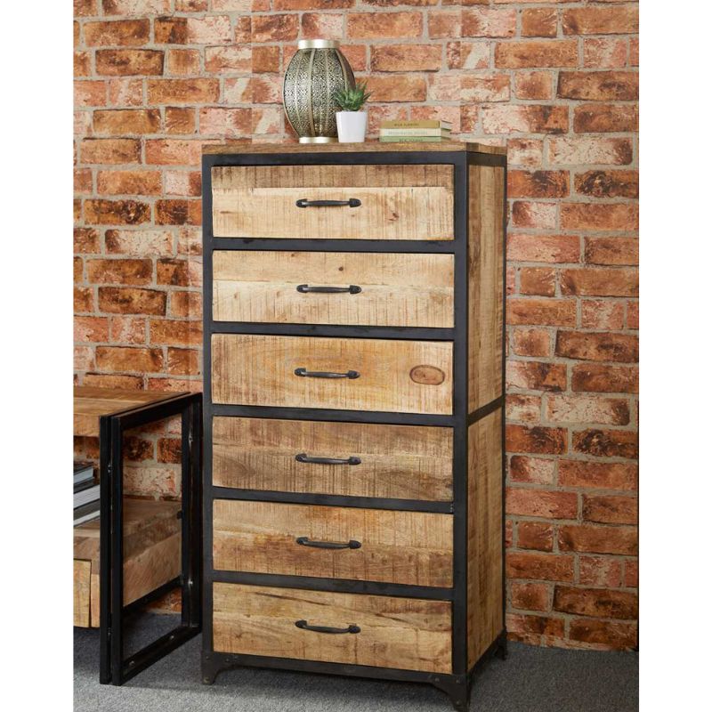 A chest of drawers made of wood in front of a brick wall.