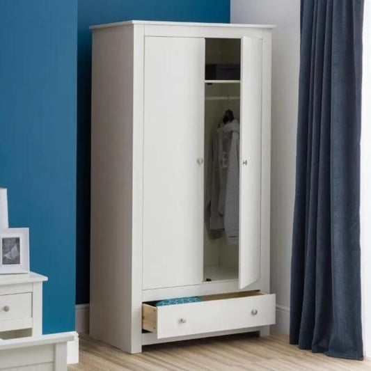 A white wardrobe featuring drawers stands against a blue wall, creating a stylish and modern interior design element.